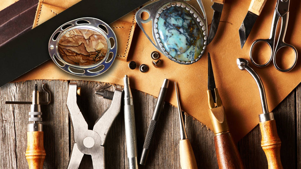 A table-top shot of leather-working tools, plus two finished hand-made belt buckles.