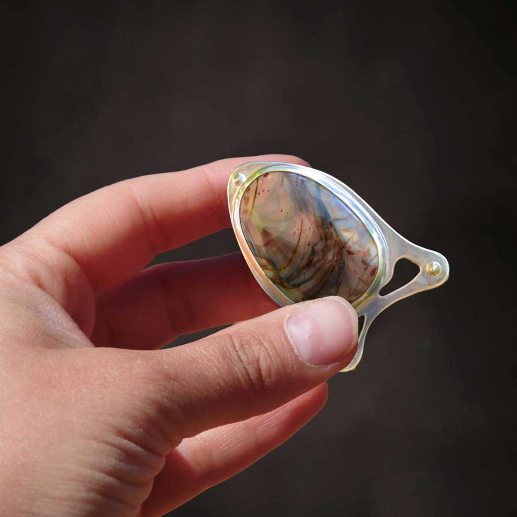 A hand holds a hand-crafted morrisonite jasper belt buckle in close-up.