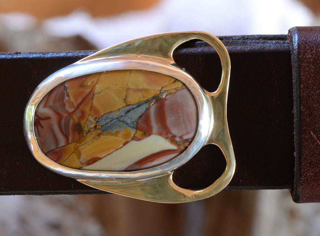 Close-up of dramatically colored red, orange, green and tan jasper cabochon in bronze belt buckle setting. Shown with brown leather belt.